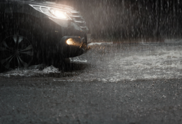 A car driving through a puddle on a dark rainy night.