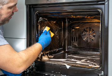 A man uses a sponge and soap to clean the inside of an oven.