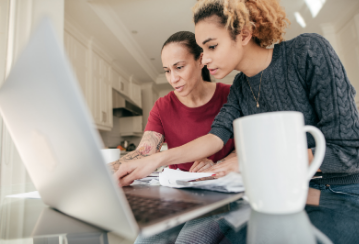 Two women reviewing something on their laptop while sitting at their kitchen table.