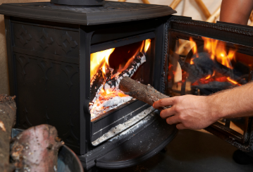 A person puts wood into a burning woodstove.