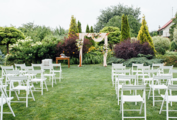 Chairs are lined up in rows facing a decorated archway in a well-groomed backyard.
