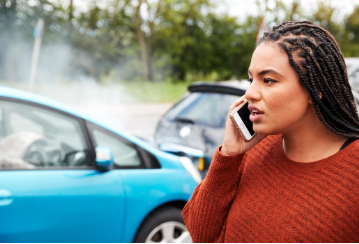 Woman on cell phone standing in front of car accident.