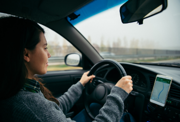 Woman driving down the road with both hands on the wheel and her phone mounted as a GPS to her dashboard.